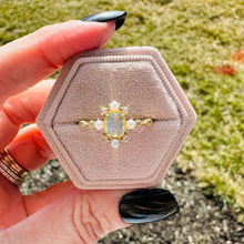 Load image into Gallery viewer, Gold ring with blue gemstone in a hexagonal pink velvet box held by a hand.