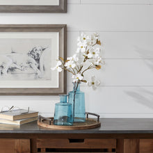 Load image into Gallery viewer, Two blue glass tapered bottle vases of different sizes placed on a wooden surface, with one vase containing white floral stems.