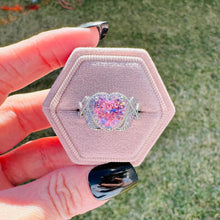 Load image into Gallery viewer, Heart-shaped ring with pink and purple glitter in a hexagonal pink velvet box held by a hand.