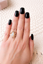 Load image into Gallery viewer, Hand with black nail polish wearing a gold ring with an opal stone on a textured white background
