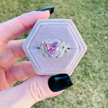 Load image into Gallery viewer, Heart-shaped pink gemstone ring in a hexagonal box held by a hand with black nail polish.
