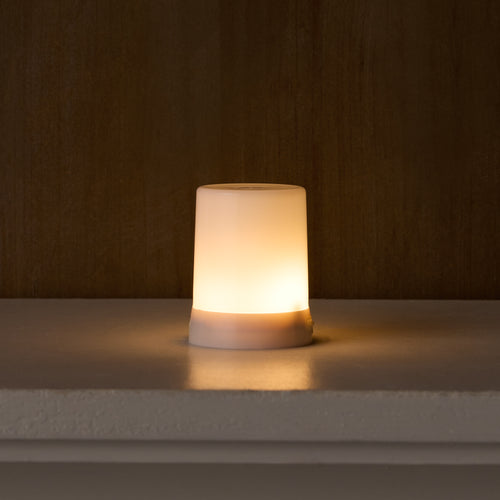 Small, round, white lamp emitting a warm glow on a dark background