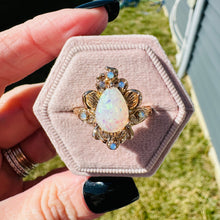 Load image into Gallery viewer, Gold ring with a large opal stone on a pink cushion, held by a hand outdoors.
