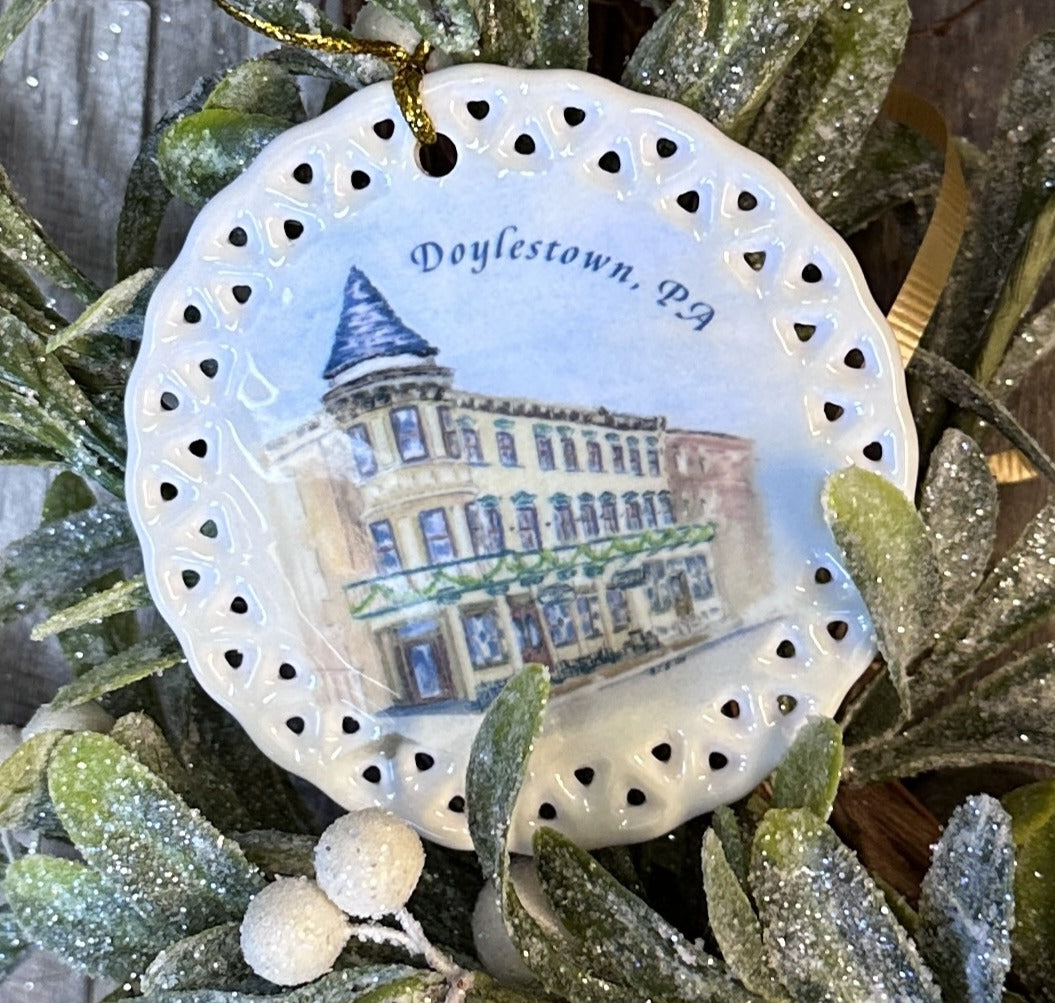 Side view of Doylestown Inn ornament in crystal-clear bag, perfect for gifting
Artist M. Catherine Bateman’s Doylestown Inn watercolor reproduced on ceramic holiday ornament, Doylestown Inn ornament displayed on Christmas tree with warm lights in background