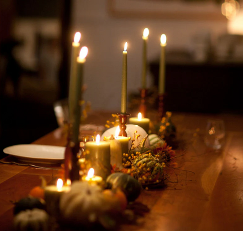 Hand-dipped bayberry taper candles burning on a dining table, surrounded by festive holiday décor